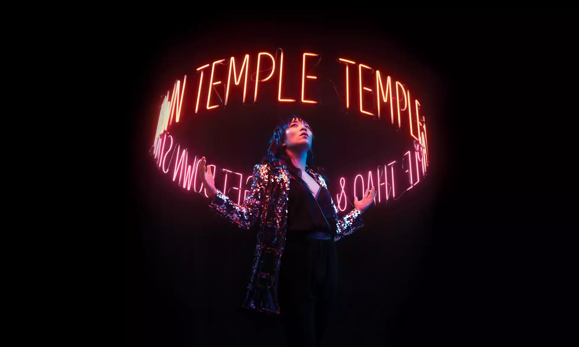 Thao standing in the dark, with a halo of neon lighting that spells out temple